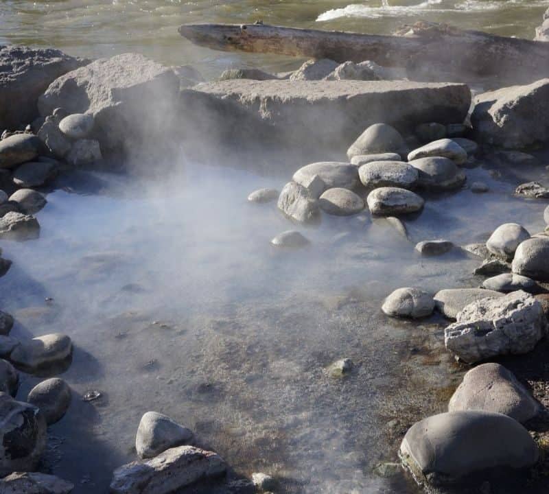 Steam rising from a natural rock-lined hot spring along a riverbank in Idaho, perfect for a relaxing weekend soak.