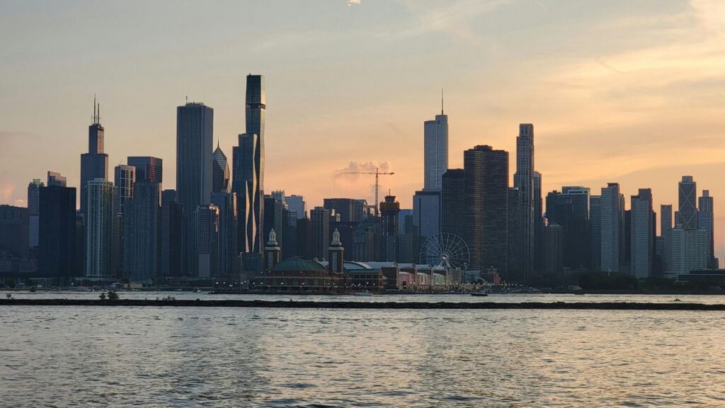 Chicago skyline at sunset with the Navy Pier and Ferris wheel in view, reflected in the calm waters of Lake Michigan.