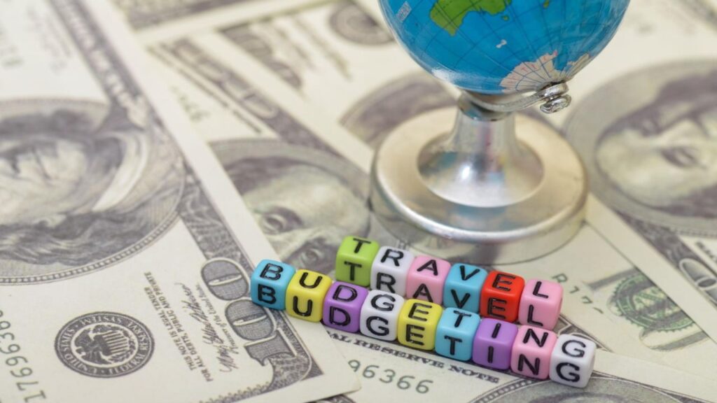 Colorful alphabet beads spelling "Travel Budgeting" placed on U.S. dollar bills with a small globe in the background