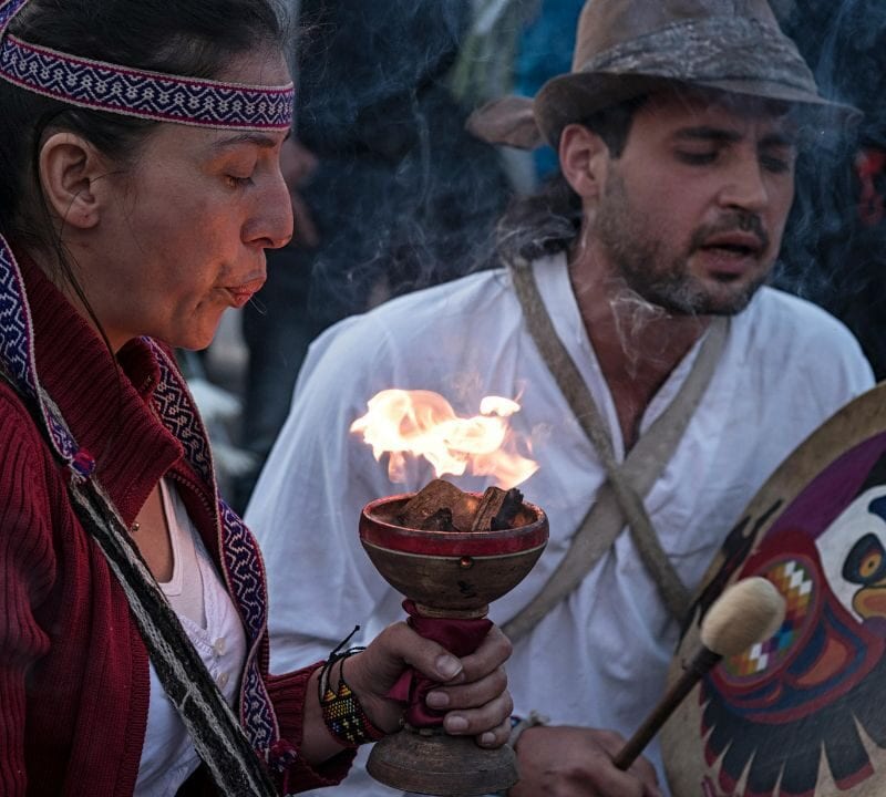 Ojibwe individuals performing a sacred smudging and drumming ritual, surrounded by smoke and ceremonial focus.