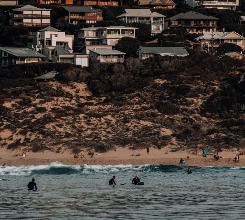 Surfers and beachgoers enjoying waves below hillside homes on California’s Central Coast.