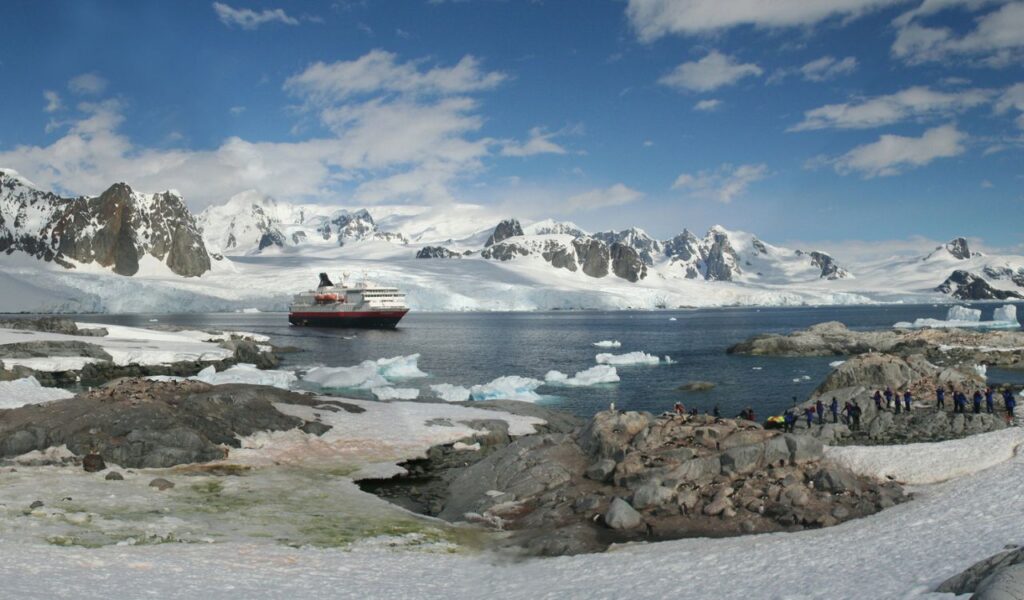 Cruise ship near icy Antarctic coast with penguins and snowy mountain backdrop.
Cruise ship near icy Antarctic coast with penguins and snowy mountain backdrop.