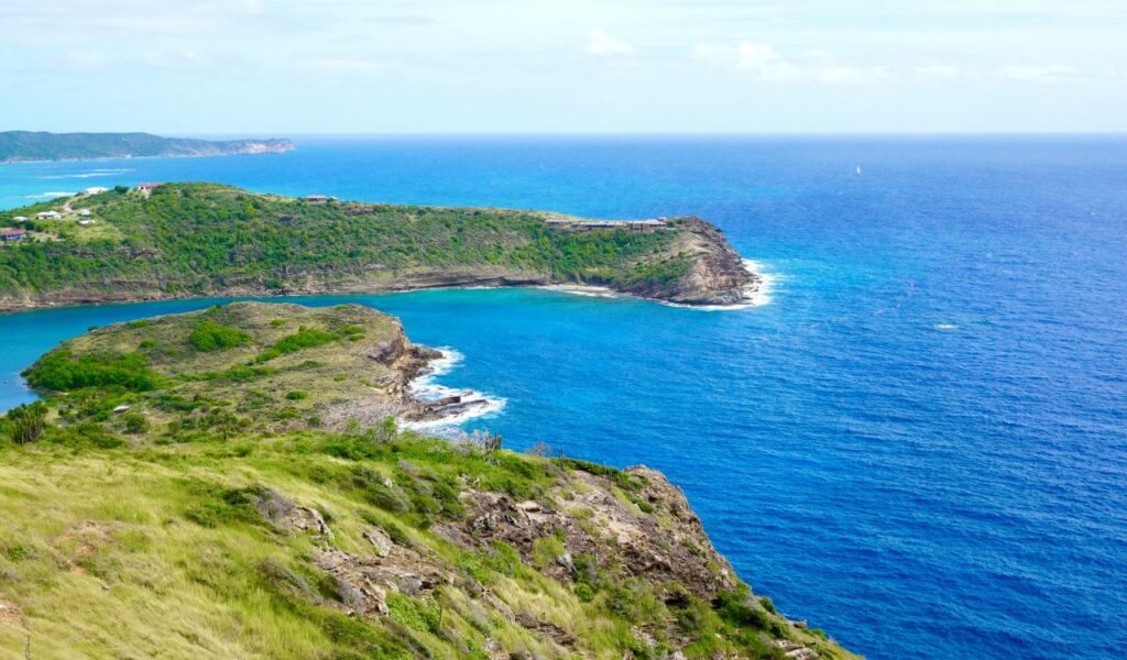 Cliffside view of a rugged peninsula and turquoise bay in Antigua, with lush greenery and deep blue Caribbean Sea.