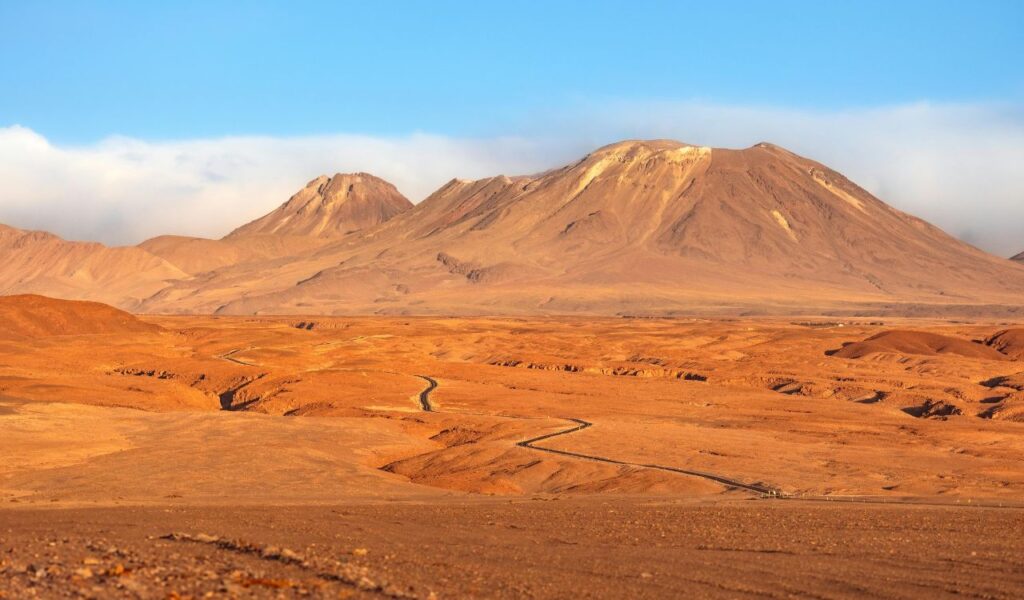 Atacama Desert in Chile with vast arid plains, winding roads, and distant mountains under a clear blue sky.