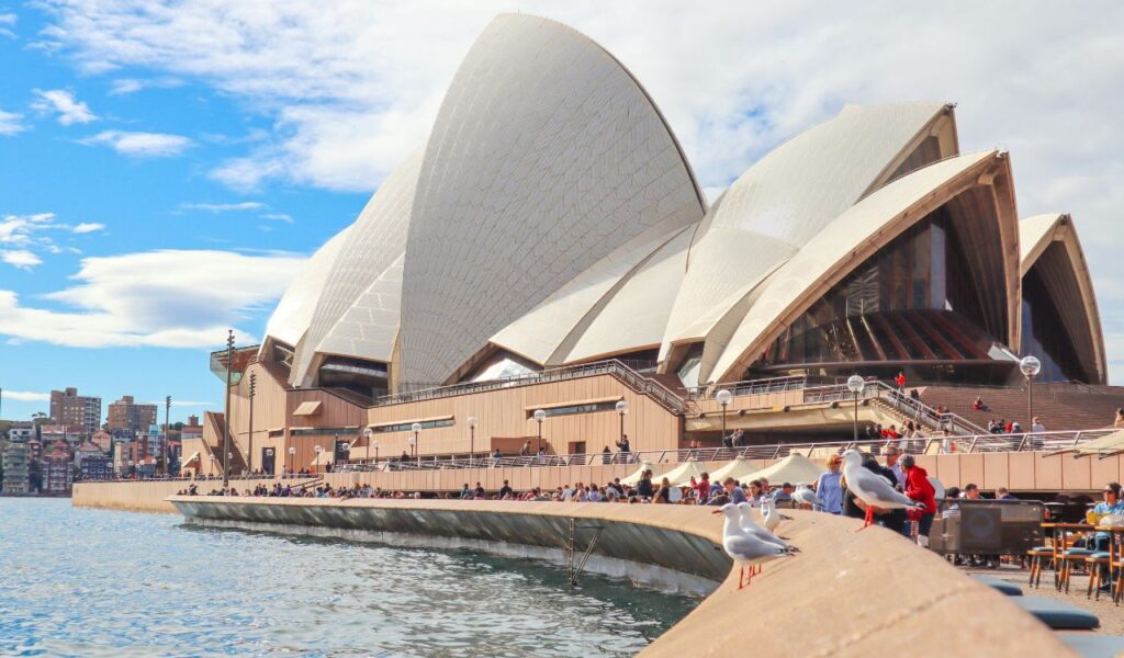 Sydney Opera House with its iconic sail-like design, viewed from the waterfront on a sunny day.