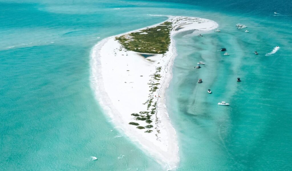 Aerial view of Bean Point Beach with its white sandy shoreline, turquoise waters, and scattered boats anchored nearby on a sunny day.