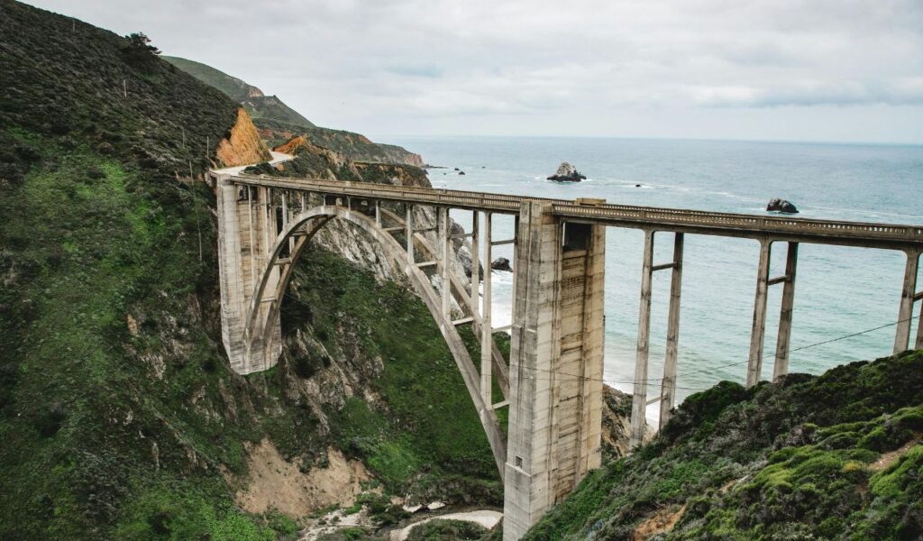 Bixby Creek Bridge stretches across a lush canyon in Big Sur, with cliffs and the Pacific Ocean in the background.