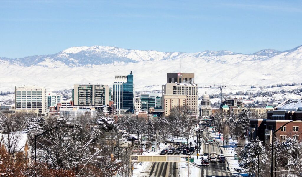Downtown Boise in winter with snow-covered streets, buildings, and mountain backdrop under a clear blue sky.