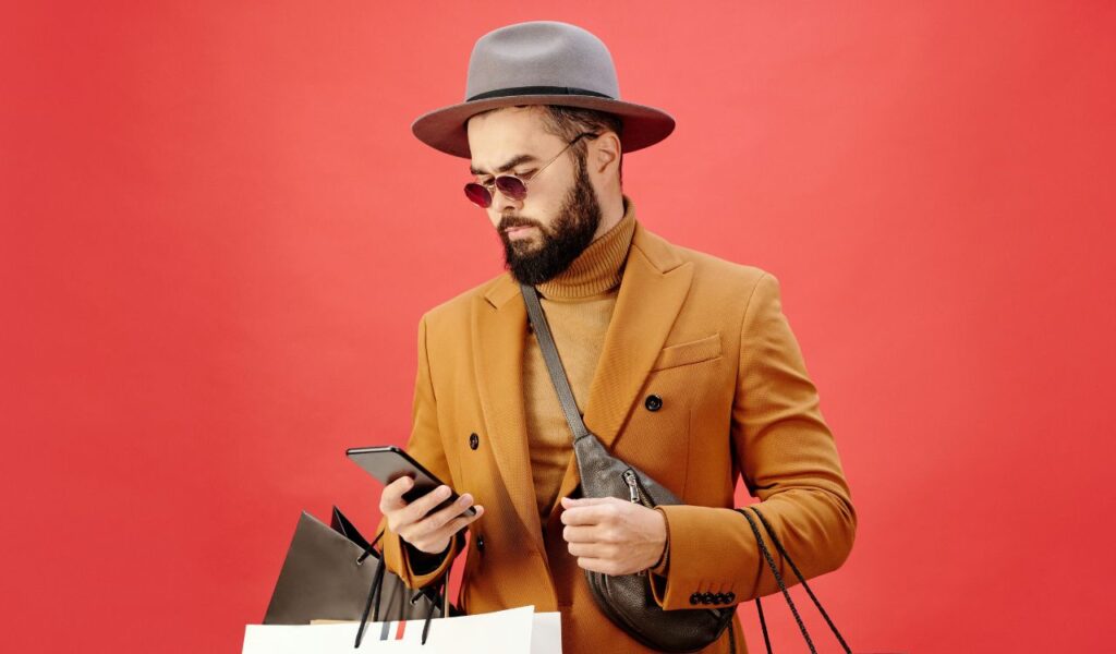 Stylish man holding shopping bags and using a smartphone, possibly checking travel deals or reward programs
