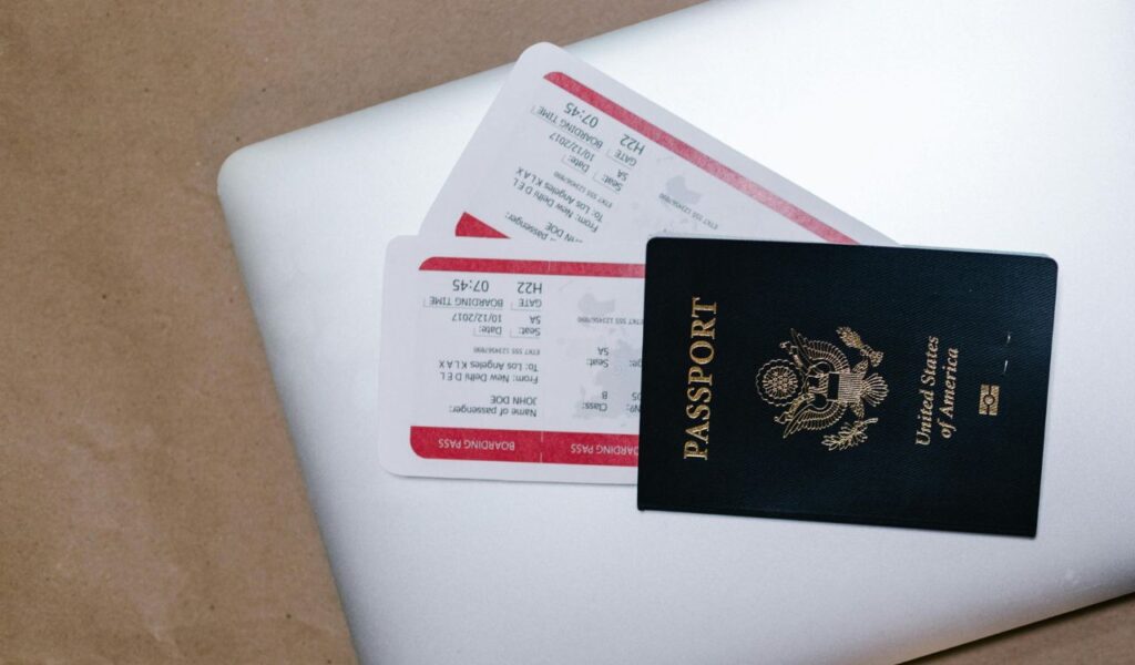 U.S. passport and airline boarding passes resting on a laptop, symbolizing travel planning and booking early