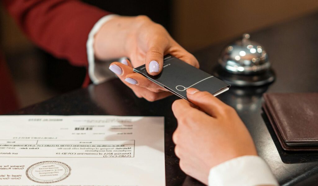 Close-up of a person handing over a passport and travel documents at a hotel reception desk, symbolizing a travel check-in process.