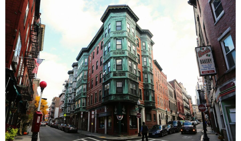 Historic brick and green-trimmed buildings line a narrow street in Boston’s North End, near Bova’s Bakery and shops.