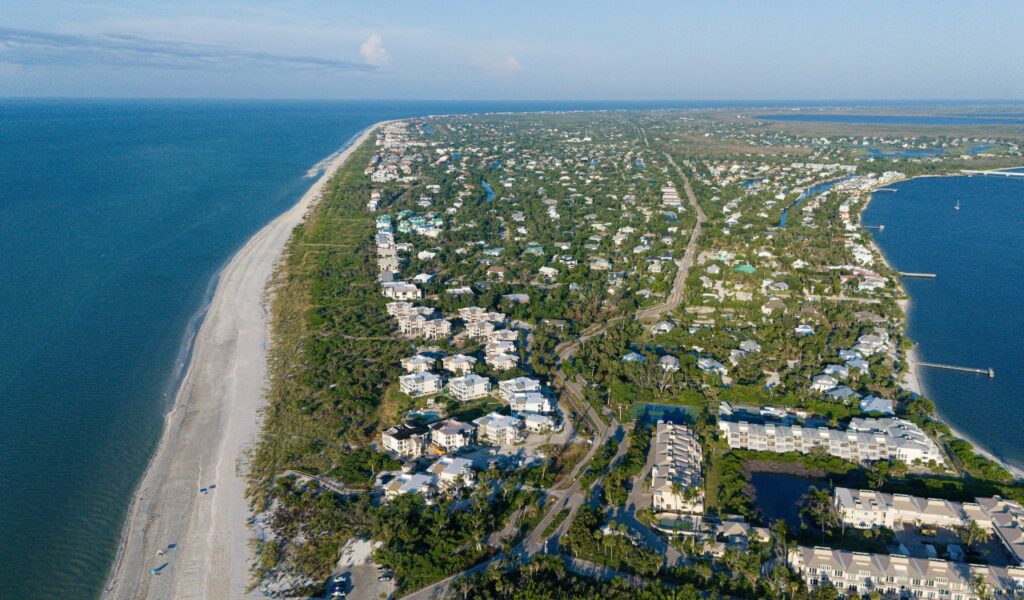 Aerial view of Caladesi Island with a long stretch of sandy beach, lush greenery, and coastal homes surrounded by calm blue waters.