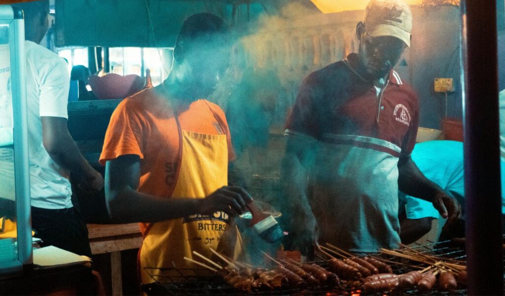 Street food vendors grilling skewered meat at a smoky night market stall in Cape Town, South Africa.