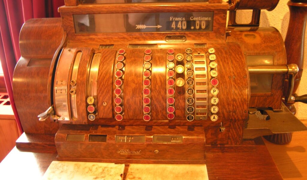 A vintage wooden cash register with round mechanical keys and a display showing "440.00 Francs" sits on a counter.