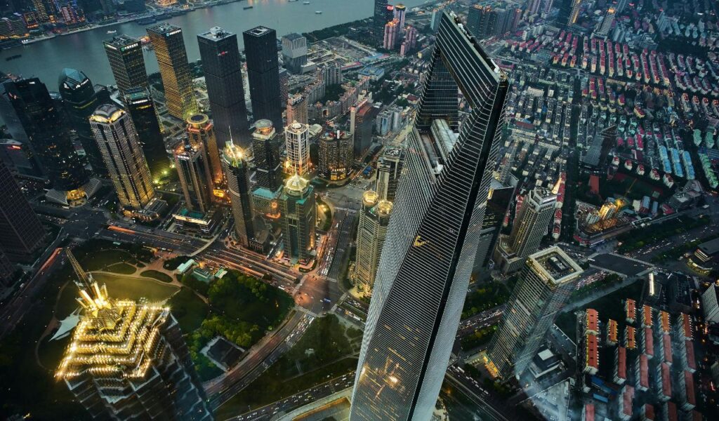 Aerial view of downtown Shanghai, China, with the brightly lit Shanghai World Financial Center and surrounding skyscrapers glowing at dusk along the Huangpu River.
