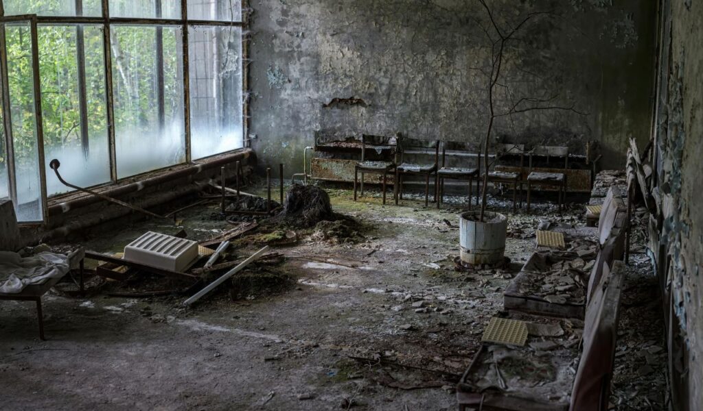 Abandoned room in Chernobyl, Ukraine, with rusted chairs, broken windows, and debris covering the cracked floor.