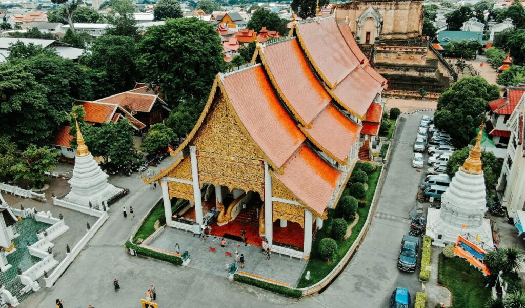 Aerial view of Wat Chedi Luang in Chiang Mai, Thailand, featuring its ornate golden temple, red-tiled roof, and surrounding white stupas.