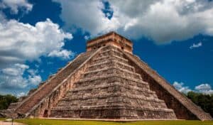 Chichén Itzá pyramid in Mexico with steep stone steps and a flat top, set against a bright blue sky with scattered clouds.