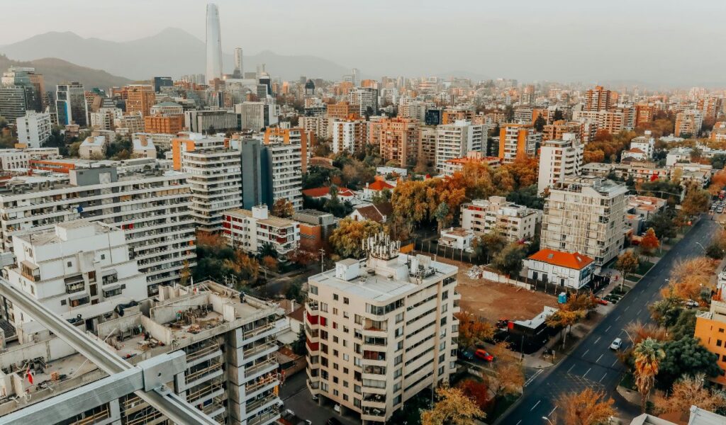 Aerial view of Santiago, Chile, featuring modern high-rise buildings, tree-lined streets, and the Andes mountains in the background