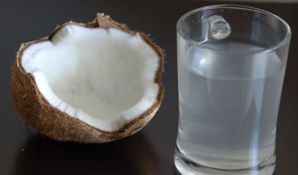 Coconut water in a glass beside a freshly opened coconut, showcasing its natural hydration benefits