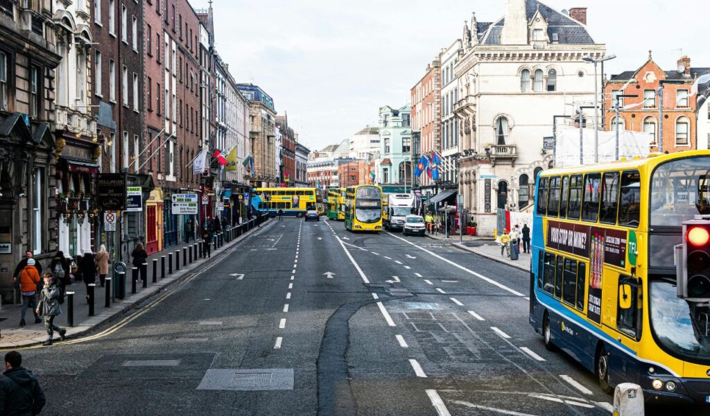 Busy city street with double-decker buses and pedestrians, highlighting affordable public transportation options.