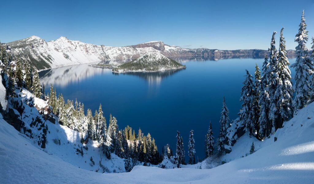 Crater Lake in Oregon surrounded by snow-covered cliffs and reflecting deep blue sky.