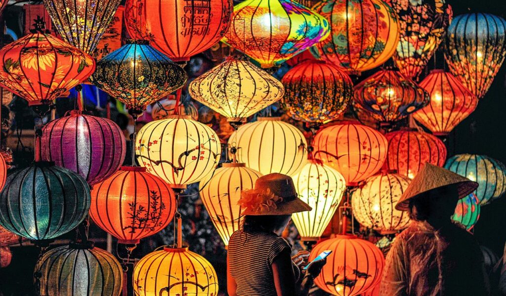 Two people admire a vibrant display of traditional Asian lanterns glowing in warm colors at night, capturing cultural richness and atmosphere.