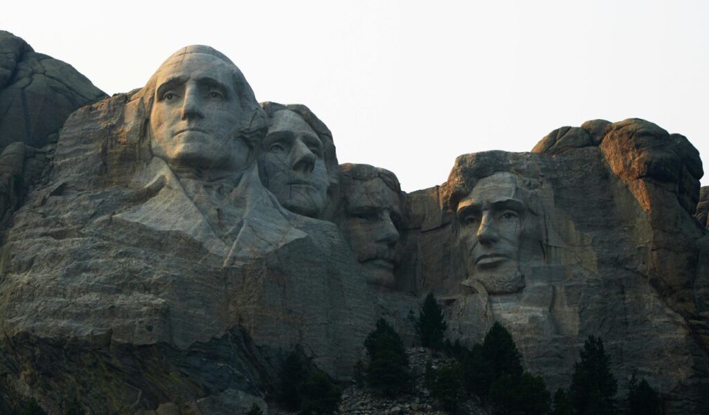 Mount Rushmore’s granite faces of four U.S. presidents emerge from the mountainside, framed by rugged rock and pine trees.