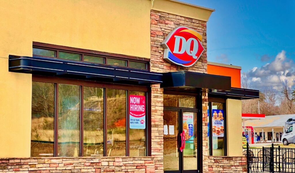 Exterior of a Dairy Queen restaurant with a 'Now Hiring' sign on the window