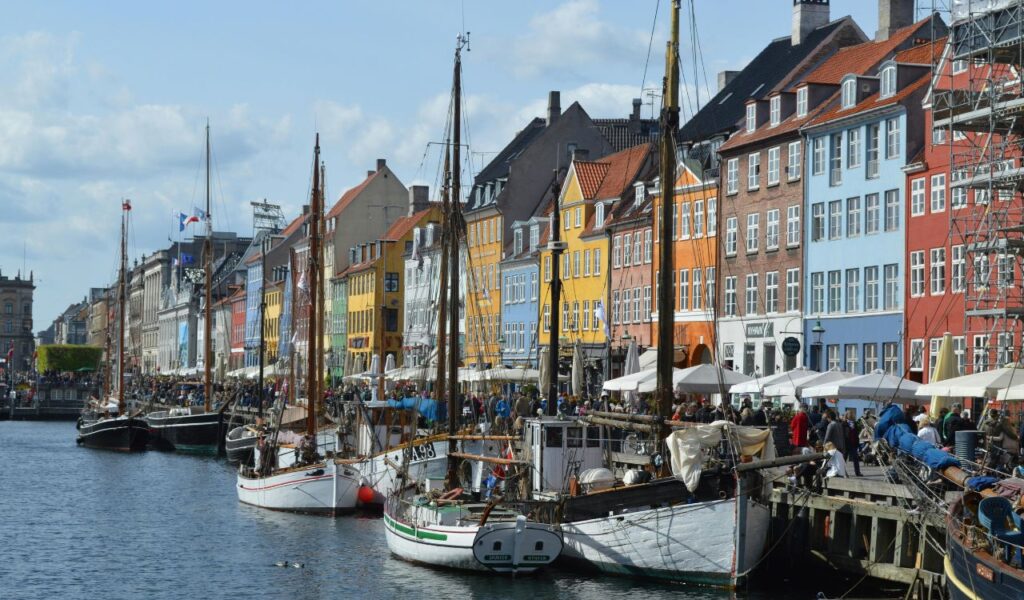 Colorful waterfront buildings and docked boats in a lively canal area in Denmark.