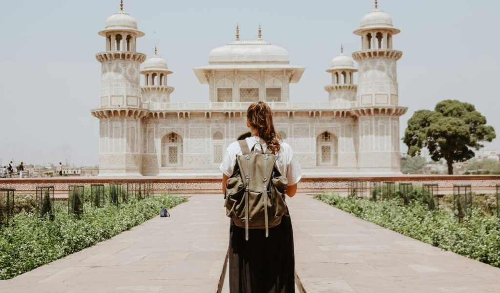 Traveler with a backpack standing in front of a historic religious site with intricate architecture and domed towers, observing respectfully from a distance