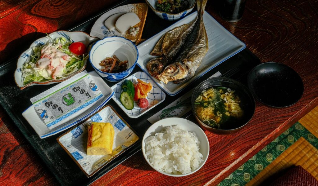 Traditional Japanese meal with grilled fish, rice, miso soup, salad, and assorted side dishes on a wooden table.