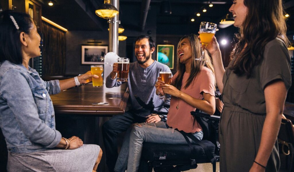 Group of friends enjoying drinks and laughing together at a bar, raising their glasses in a cheerful toast.