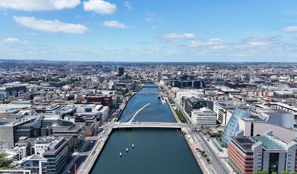 Aerial view of modern Dublin, Ireland, with the River Liffey running through the city and the Samuel Beckett Bridge in the foreground.