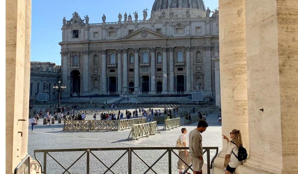 Tourists arriving early at St. Peter’s Square with a view of St. Peter’s Basilica façade, scattered visitors, and clear morning light.