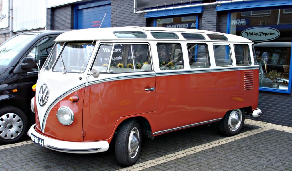 Vintage red and white Volkswagen bus parked outside an auto repair shop, showcasing a classic road trip vehicle.