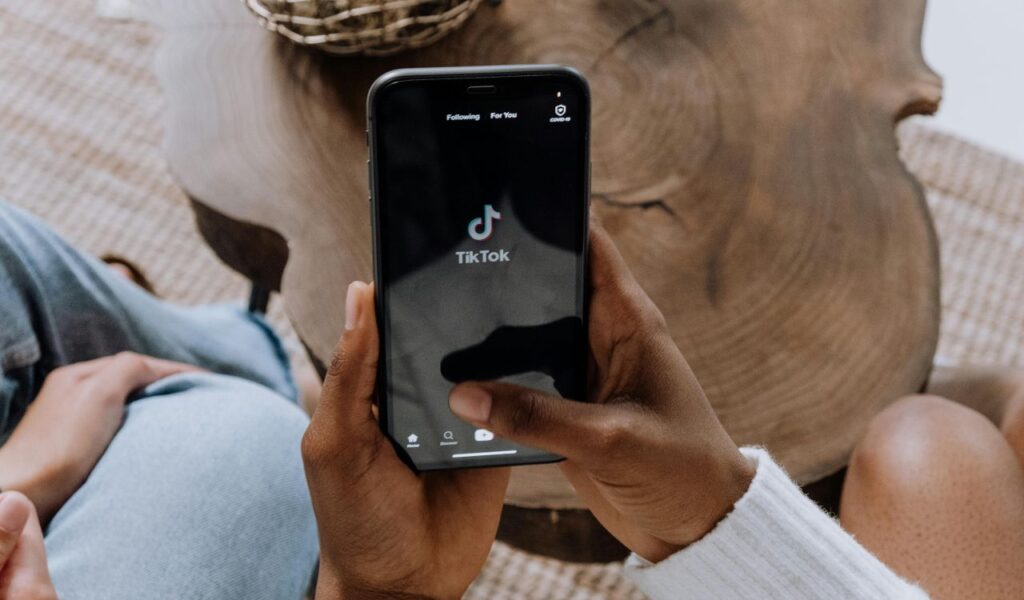 A person holding a smartphone with the TikTok app open while sitting in a casual living room setting beside a wooden coffee table.