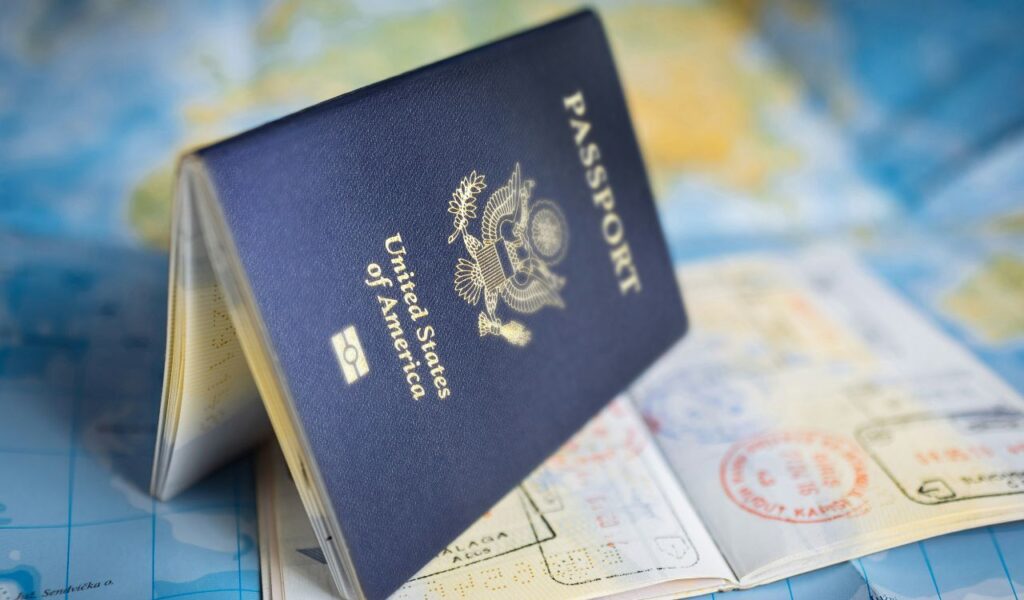 A United States passport standing open on top of a page filled with international entry and exit stamps, placed over a world map background.