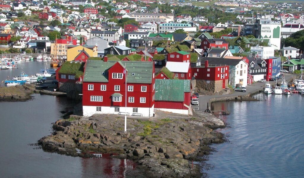 Colorful waterfront buildings with grass roofs in Tórshavn, Faroe Islands, surrounded by boats and rocky coastline.