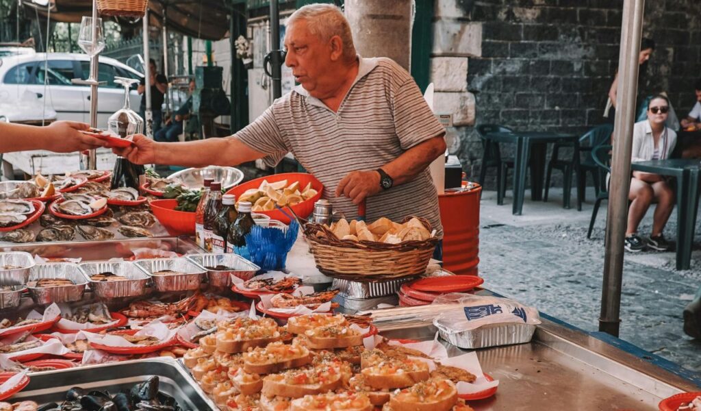 A street vendor in Florence serving seafood and bruschetta at an outdoor market stall with fresh dishes displayed on the counter.