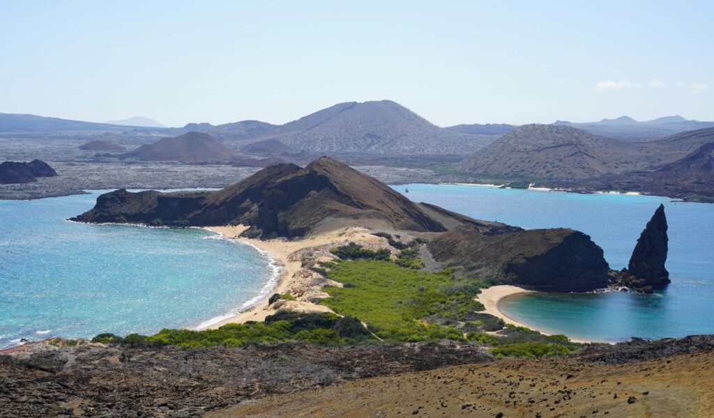 Scenic view of the Galápagos Islands, Ecuador, with volcanic hills, turquoise waters, sandy beaches, and rocky coastline.