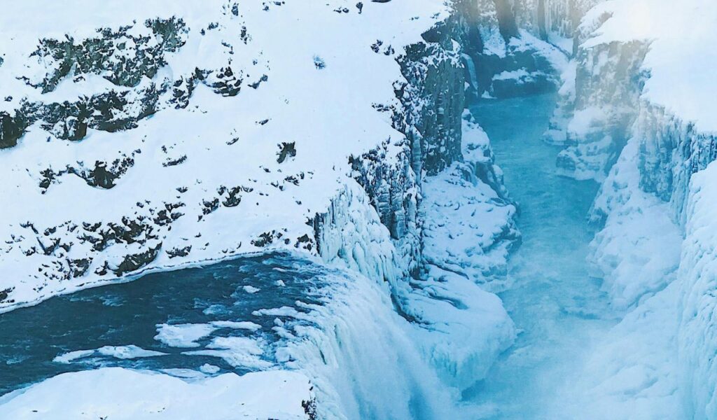A frozen river cutting through steep cliffs at Partnach Gorge in winter, with snow-covered rocks and icy formations along the edges of the gorge.