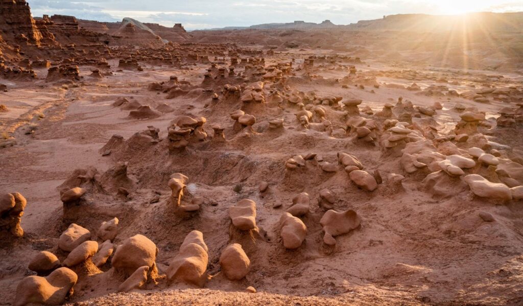Sunlight shines over a surreal desert landscape filled with mushroom-shaped rock formations in Goblin Valley State Park.