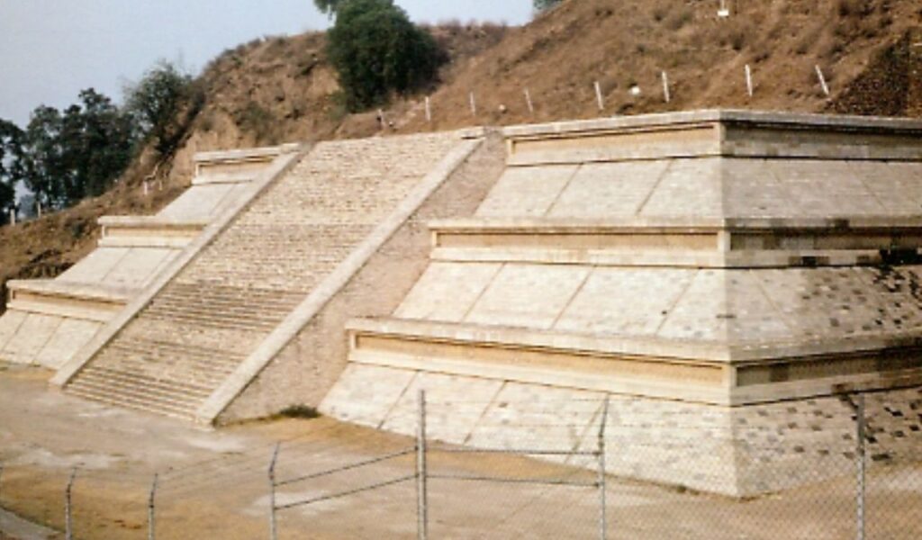 Restored steps of the Great Pyramid of Cholula in Mexico, with fenced access and a hillside rising behind the structure.