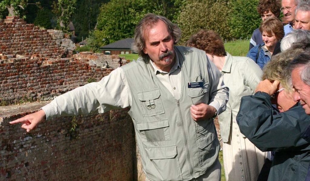 A tour guide gestures while leading a group of visitors near historic brick ruins in an outdoor walking tour.
