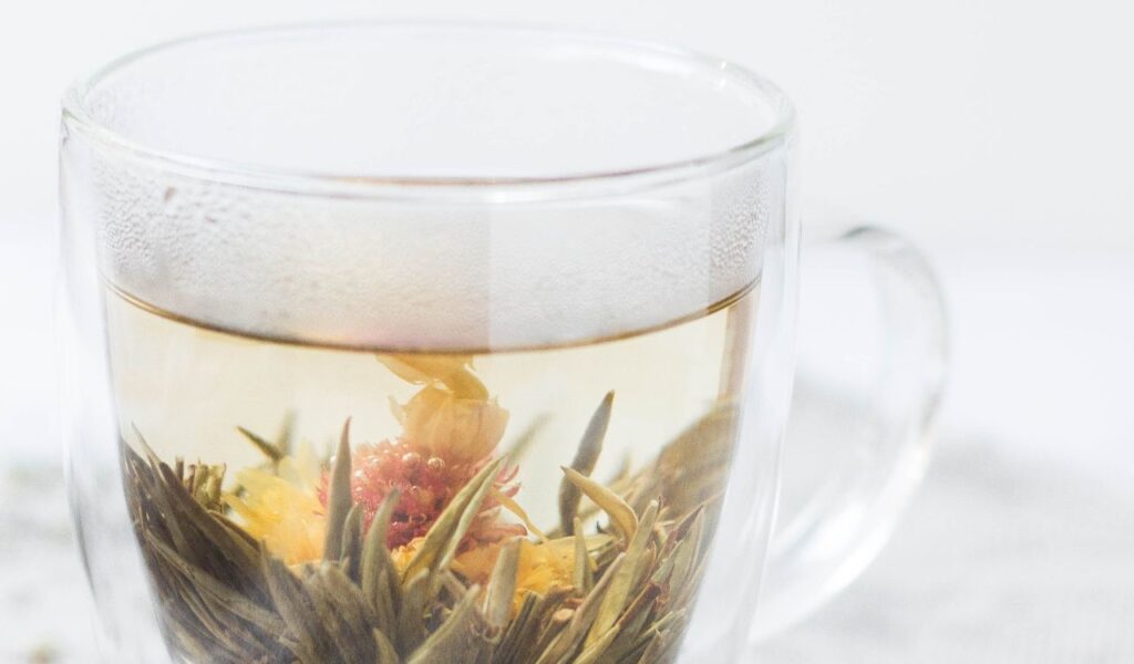 Herbal tea in a clear cup, with blooming flowers and leaves, showcasing a calming infusion