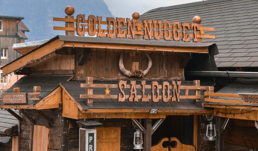Rustic wooden building with a sign that reads "Golden Nugget Saloon" and features Western-style decor including a mounted bull skull and swinging saloon doors.