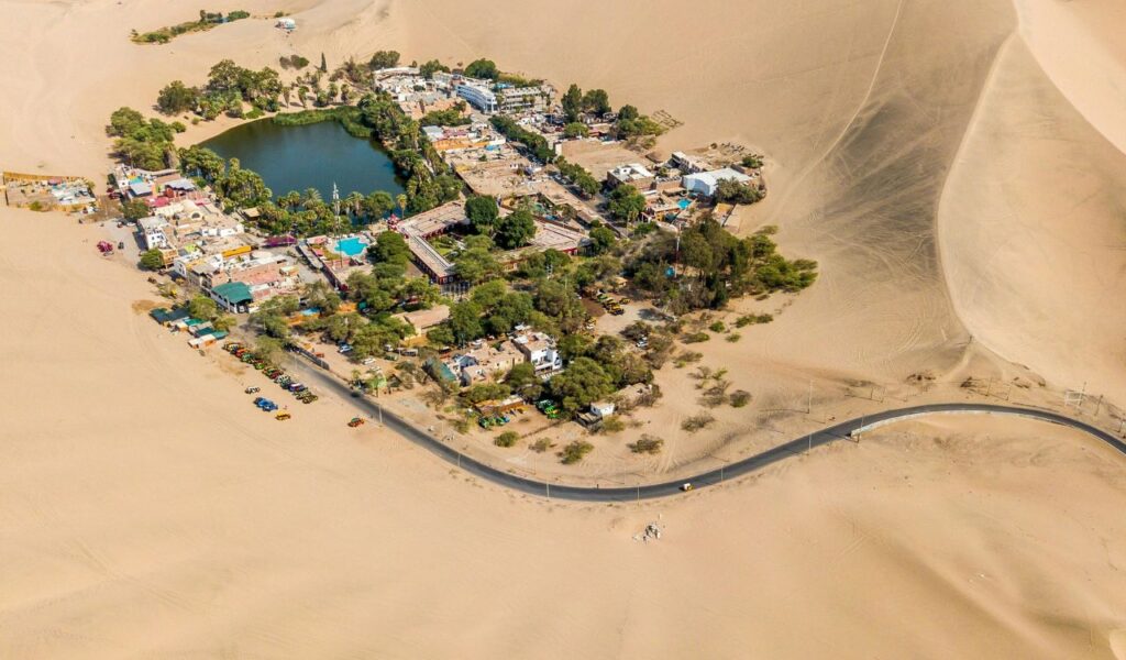 Huacachina oasis in Peru surrounded by desert sand dunes with a lagoon and small village in the center.