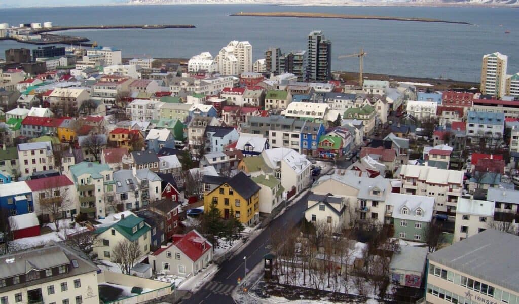 Aerial view of Reykjavík with colorful rooftops, modern buildings, and a snowy coastline along the North Atlantic.